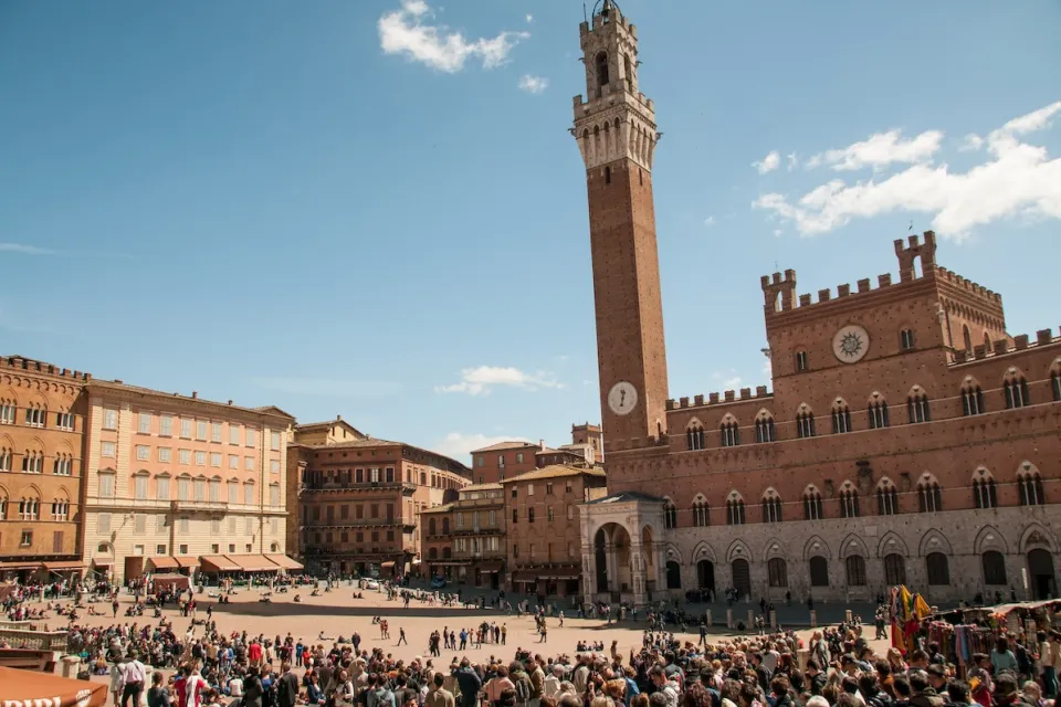 Busy plaza in Siena, Italy with prominent clock tower.